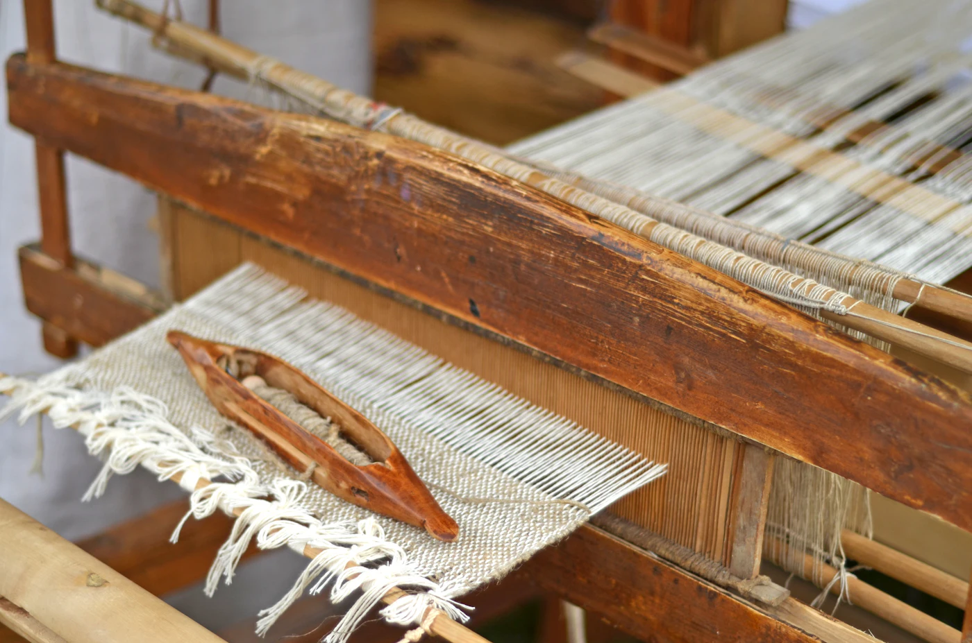 A wooden shuttle resting on cloth on the loom