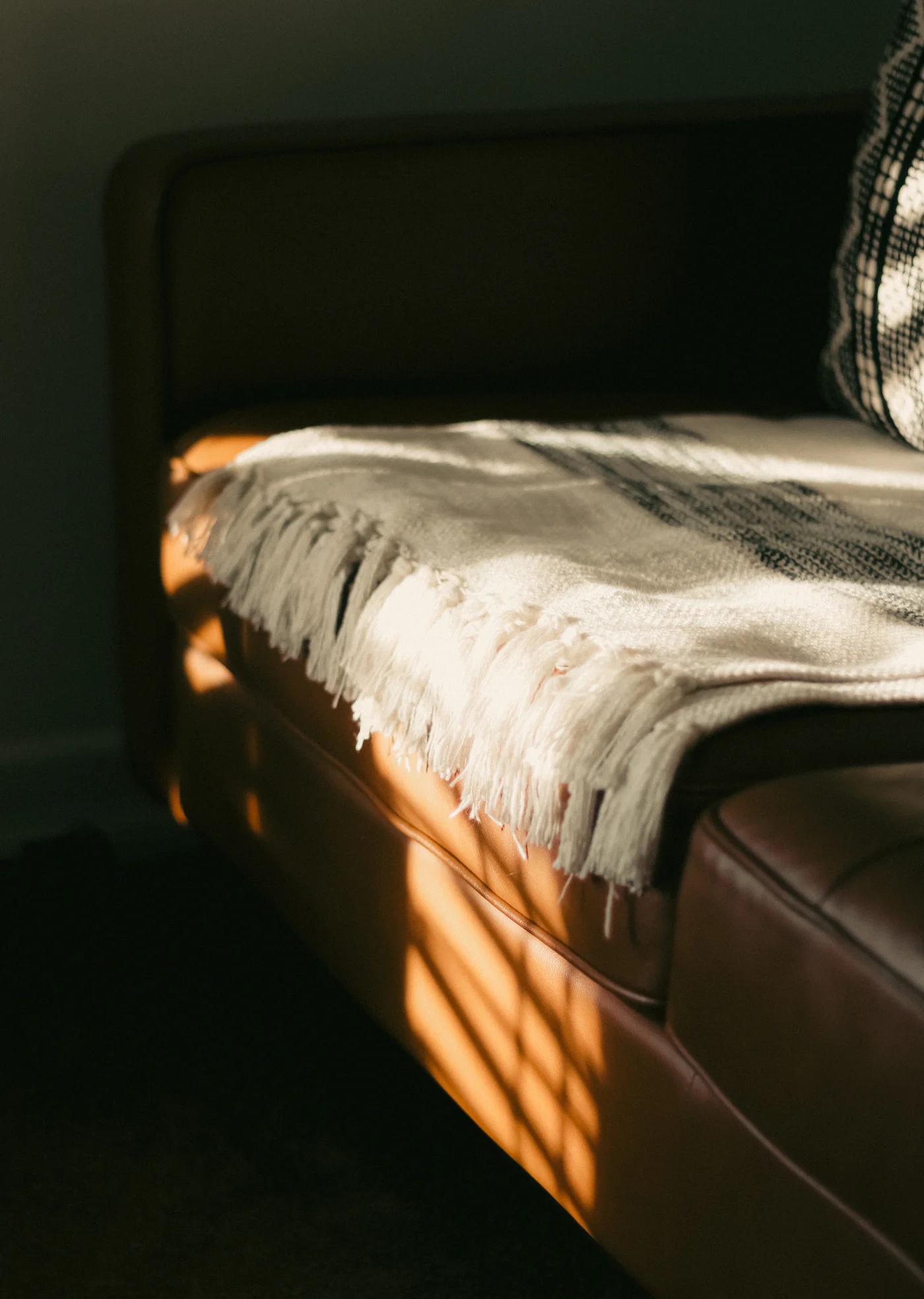 A cream throw folded over a leather sofa in afternoon light